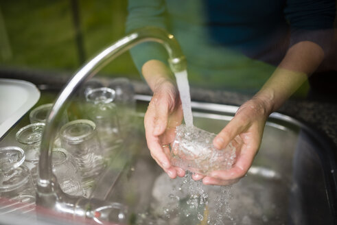 Woman washing glasses at kitchen sink - RAEF001180