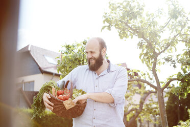 Young man standing in garden, basket with fresh vegetables - SEGF000553