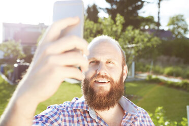 Junger Mann mit Smartphone im Garten, Selfie - SEGF000567