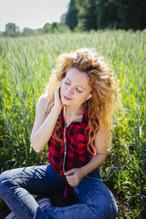 Portrait of woman sitting in a field hearing music with earphones - GIOF001133