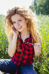 Porträt einer Frau, die auf einem Feld sitzt und mit Kopfhörern Musik hört - GIOF001135