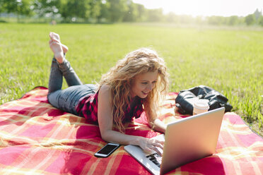 Woman lying on blanket on a meadow using laptop - GIOF001152