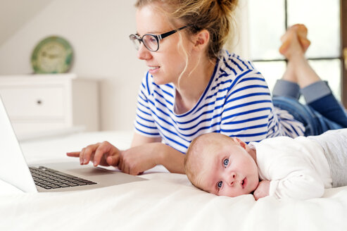 Mutter mit Baby auf dem Bett liegend und mit Laptop arbeitend - HAPF000454