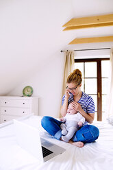 Mutter mit Baby zu Hause bei der Arbeit mit Laptop - HAPF000456