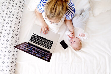 Mutter mit Baby zu Hause bei der Arbeit mit Laptop - HAPF000458