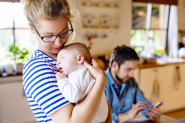 Mutter hält kleines Baby mit Vater im Hintergrund - HAPF000463