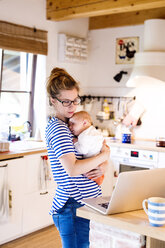 Mutter mit Baby in der Küche mit Blick auf den Laptop - HAPF000466