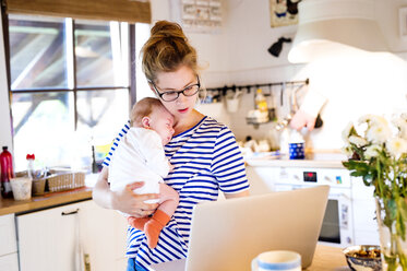 Mother with baby in kitchen looking at laptop - HAPF000467