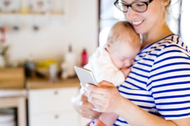 Mutter hält kleines Baby und schaut auf ihr Handy - HAPF000471