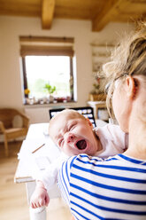 Mother at home holding crying baby - HAPF000474