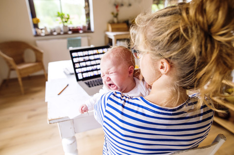 Mutter am Schreibtisch zu Hause mit weinendem Baby, lizenzfreies Stockfoto