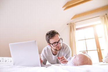 Vater mit Baby auf dem Bett liegend mit Laptop - HAPF000478