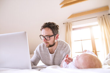 Father with baby lying on bed using laptop - HAPF000479