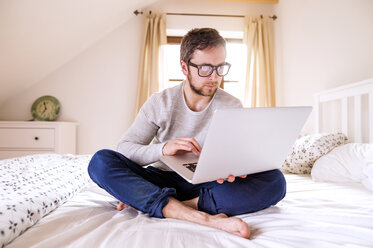 Mann sitzt auf dem Bett und benutzt einen Laptop - HAPF000482