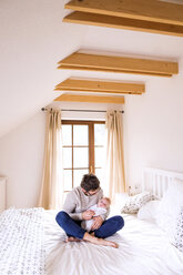 Father with baby sitting on bed - HAPF000483