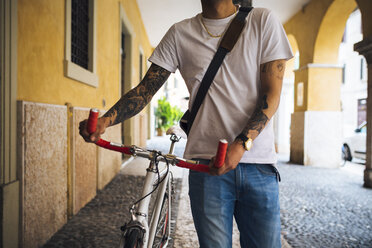 Junger Mann zu Fuß mit einem Fahrrad in der Stadt - GIOF001160