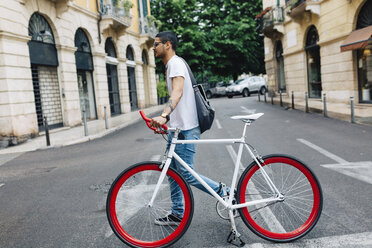 Junger Mann zu Fuß mit einem Fahrrad in der Stadt - GIOF001165