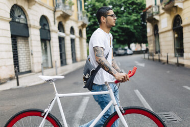 Junger Mann zu Fuß mit einem Fahrrad in der Stadt - GIOF001166