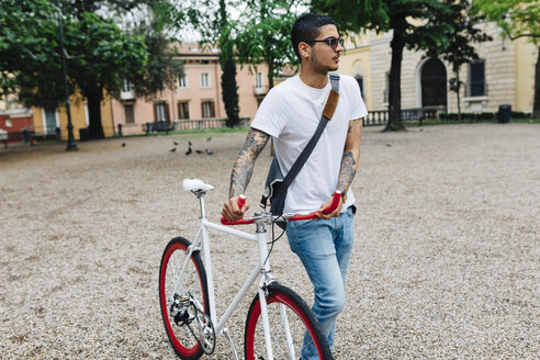Junger Mann zu Fuß mit einem Fahrrad in der Stadt - GIOF001168