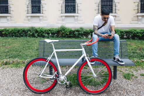 Junger Mann mit einem Fahrrad auf einer Bank sitzend - GIOF001170