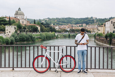 Italy, Verona, young man with a bicycle standing on a bridge - GIOF001179