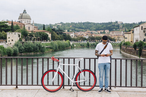 Italien, Verona, junger Mann mit Fahrrad auf einer Brücke stehend - GIOF001179