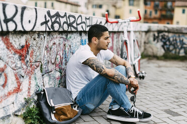 Junger Mann sitzt an einer Graffiti-Wand - GIOF001182