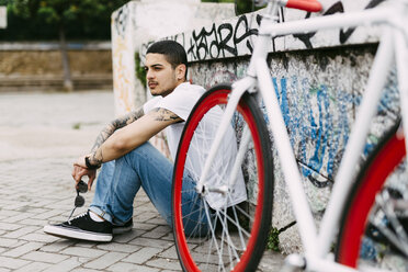Junger Mann sitzt an einer Graffiti-Wand - GIOF001184