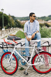 Junger Mann mit einem Fahrrad auf einer Graffiti-Wand sitzend - GIOF001185