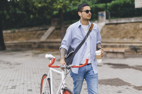 Junger Mann zu Fuß mit einem Fahrrad in der Stadt - GIOF001189
