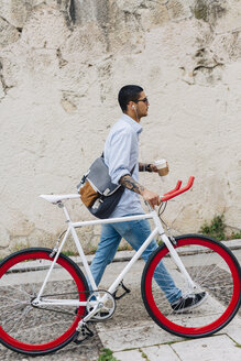 Junger Mann zu Fuß mit einem Fahrrad in der Stadt - GIOF001190