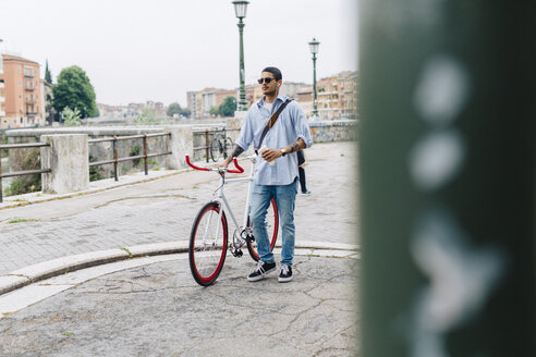 Junger Mann zu Fuß mit einem Fahrrad in der Stadt - GIOF001191