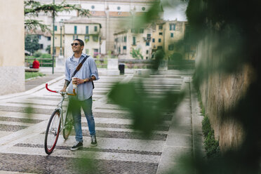 Junger Mann zu Fuß mit einem Fahrrad in der Stadt - GIOF001192