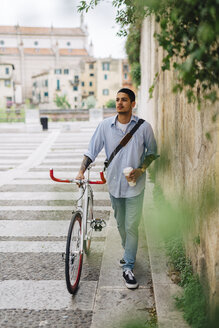 Junger Mann zu Fuß mit einem Fahrrad in der Stadt - GIOF001194