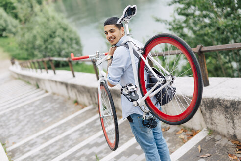 Junger Mann trägt ein Fahrrad auf einer Treppe - GIOF001196