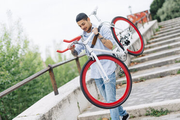 Junger Mann trägt ein Fahrrad auf einer Treppe - GIOF001197