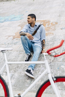 Junger Mann mit einem Fahrrad auf einer Mauer sitzend - GIOF001199