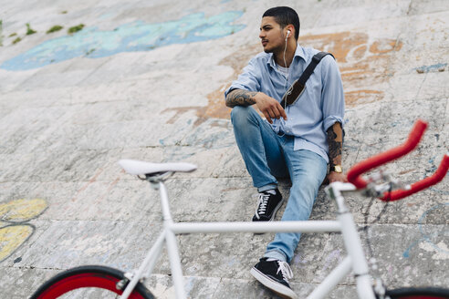 Junger Mann mit einem Fahrrad auf einer Mauer sitzend - GIOF001200