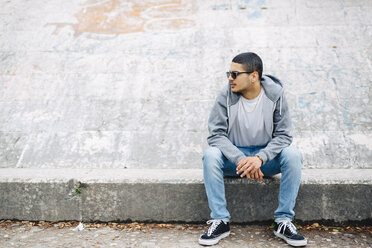 Young man sitting on a wall wearing a hoodie - GIOF001203