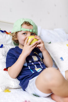 Kleiner Junge sitzt auf der Couch und isst einen Apfel - MGOF001888