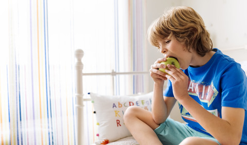 Porträt eines Jungen, der auf der Couch sitzt und einen Apfel isst, lizenzfreies Stockfoto