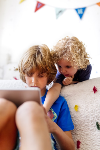 Zwei kleine Brüder benutzen ein Tablet zu Hause, lizenzfreies Stockfoto