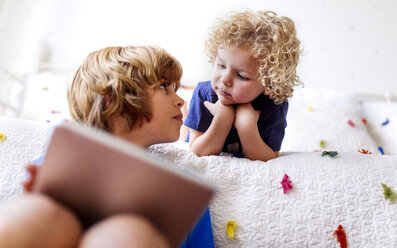 Two little brothers with tablet at home looking each other - MGOF001901