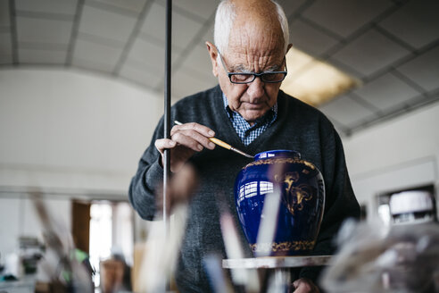 Senior man decorating ceramic vase in his spare time - JRFF000686