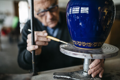 Senior man decorating ceramic vase in his spare time - JRFF000687