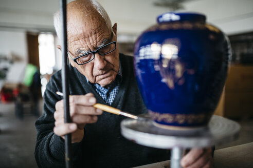 Senior man decorating ceramic vase in his spare time - JRFF000688