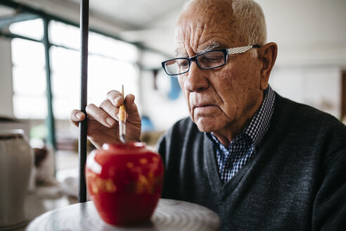 Senior man decorating ceramic vase in his spare time - JRFF000690