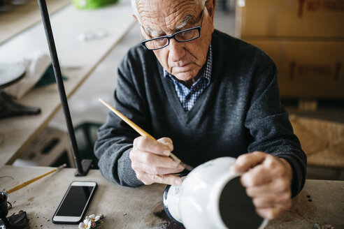 Senior man decorating ceramic vase in his spare time - JRFF000701