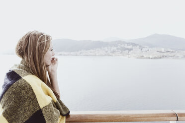 Blonde Frau mit Decke an Deck eines Kreuzfahrtschiffes, die in die Ferne schaut - ONBF000036