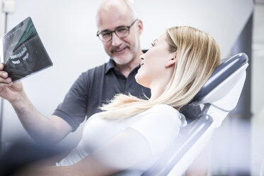 Zahnarzt zeigt dem Patienten, der im Zahnarztstuhl sitzt, ein Röntgenbild - FMKF002634